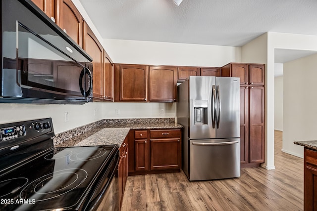 kitchen featuring dark stone counters, black appliances, and wood-type flooring