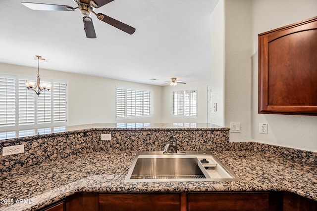 kitchen with a sink, dark stone counters, decorative light fixtures, and a chandelier