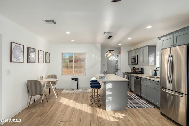 kitchen with a center island, stainless steel appliances, decorative light fixtures, and light hardwood / wood-style flooring