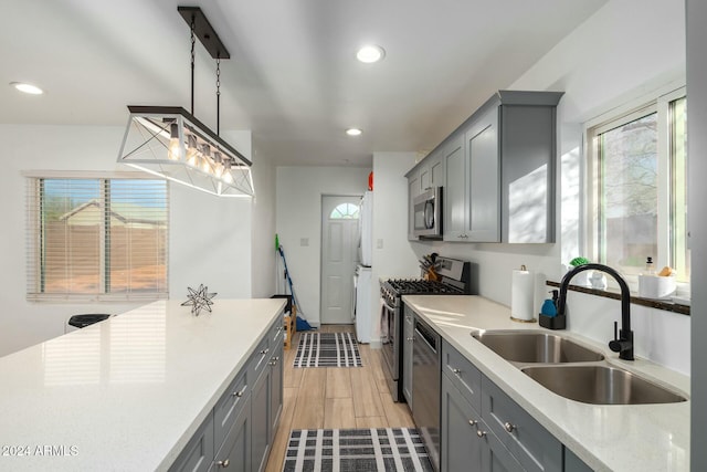 kitchen with gray cabinetry, stainless steel appliances, sink, decorative light fixtures, and light hardwood / wood-style floors