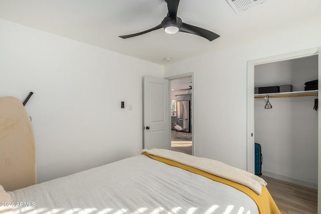 bedroom with hardwood / wood-style floors, ceiling fan, stainless steel fridge, and a closet