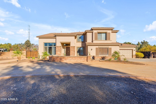 view of front of home featuring stucco siding, fence, a garage, stone siding, and driveway