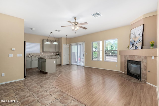 kitchen with ceiling fan, gray cabinetry, hanging light fixtures, a kitchen island, and a tiled fireplace