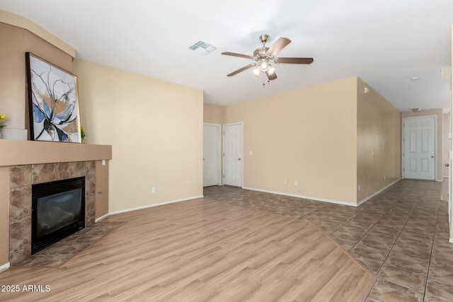 unfurnished living room with a tiled fireplace, hardwood / wood-style floors, and ceiling fan