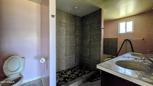 bathroom featuring toilet, tiled shower, double vanity, and a sink