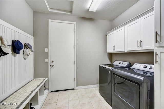 laundry area with washing machine and dryer, a textured ceiling, cabinets, and light tile patterned floors