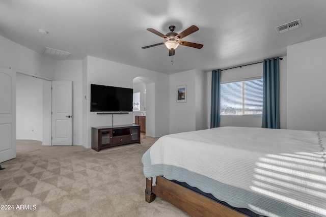 bedroom featuring ceiling fan, light carpet, and ensuite bath