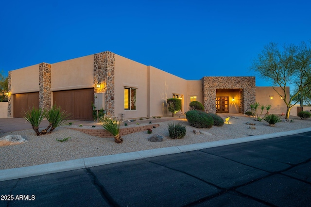 southwest-style home with a garage, stone siding, driveway, and stucco siding