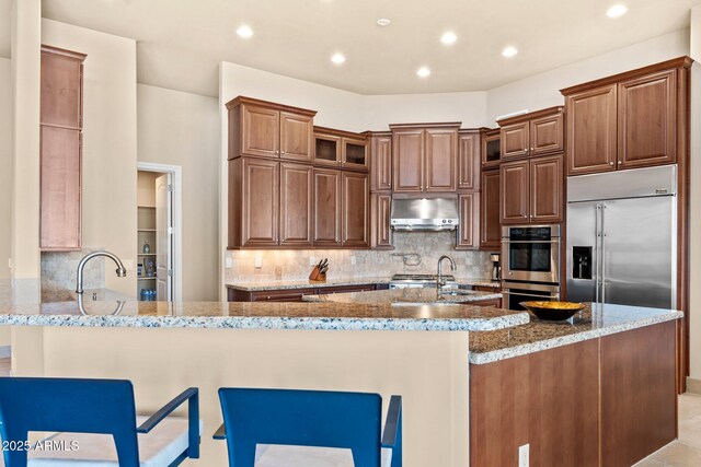 kitchen featuring light stone counters, appliances with stainless steel finishes, ventilation hood, and a peninsula