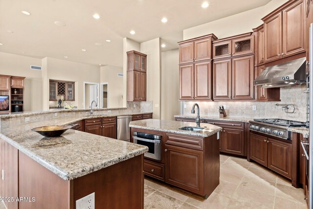 kitchen with a kitchen island with sink, stainless steel appliances, under cabinet range hood, and a sink