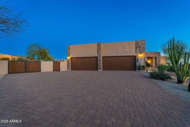 view of front of house featuring a gate, stucco siding, a garage, stone siding, and decorative driveway