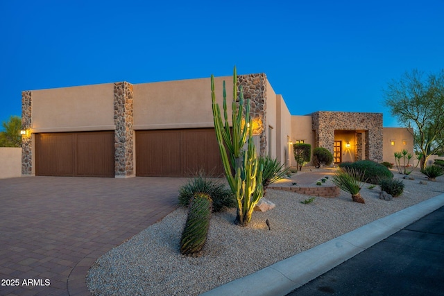 pueblo-style home featuring stucco siding, stone siding, and a garage