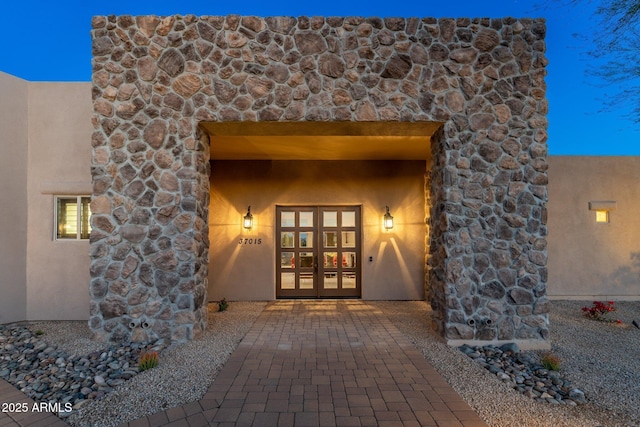 entrance to property with french doors, stone siding, and stucco siding