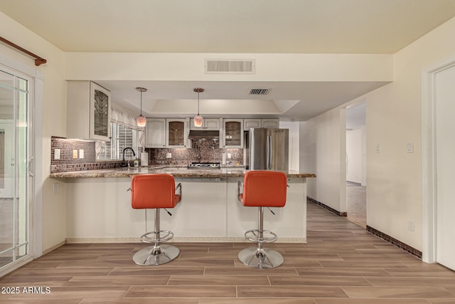 kitchen with pendant lighting, backsplash, a kitchen breakfast bar, kitchen peninsula, and stainless steel refrigerator