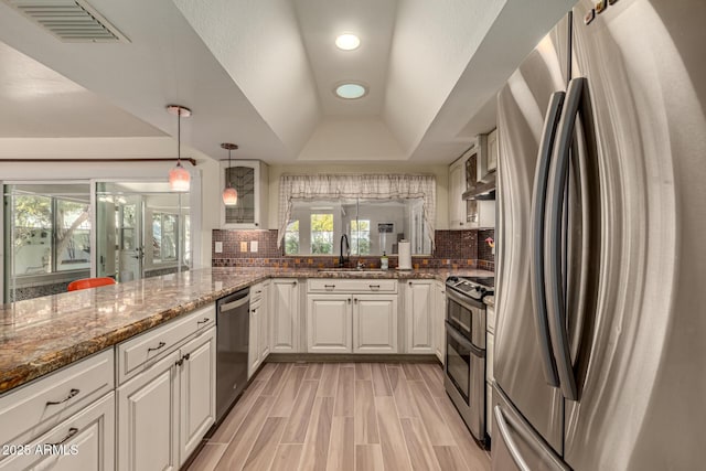 kitchen featuring kitchen peninsula, appliances with stainless steel finishes, a tray ceiling, sink, and white cabinetry