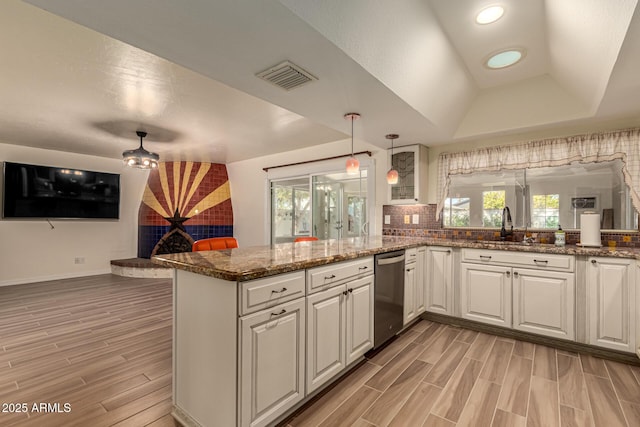 kitchen with a raised ceiling, kitchen peninsula, dishwasher, and white cabinets