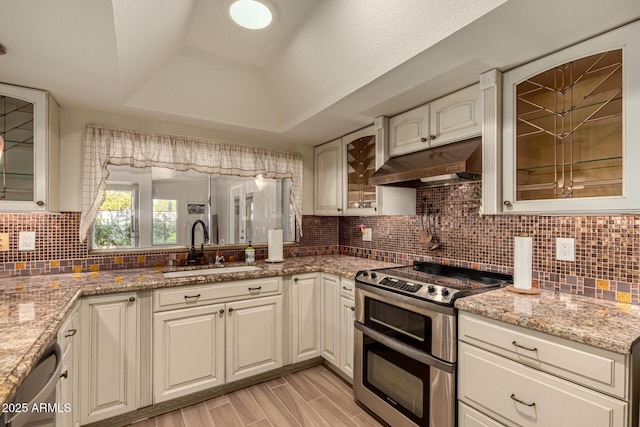 kitchen with light stone countertops, sink, backsplash, a tray ceiling, and appliances with stainless steel finishes