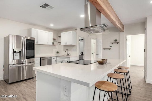 kitchen featuring a breakfast bar, a sink, visible vents, appliances with stainless steel finishes, and wall chimney range hood