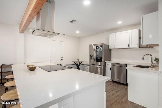 kitchen featuring a breakfast bar area, visible vents, appliances with stainless steel finishes, a sink, and wall chimney range hood