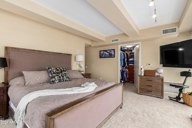 bedroom with a closet, light colored carpet, a walk in closet, and beamed ceiling