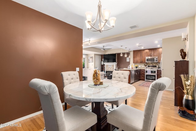 dining space featuring ceiling fan with notable chandelier, a stone fireplace, and light hardwood / wood-style flooring