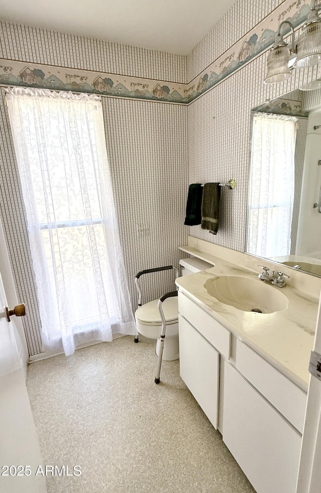 bathroom with toilet, vanity, and wallpapered walls