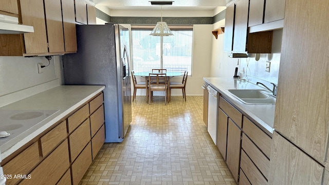 kitchen with under cabinet range hood, a sink, light countertops, appliances with stainless steel finishes, and decorative light fixtures