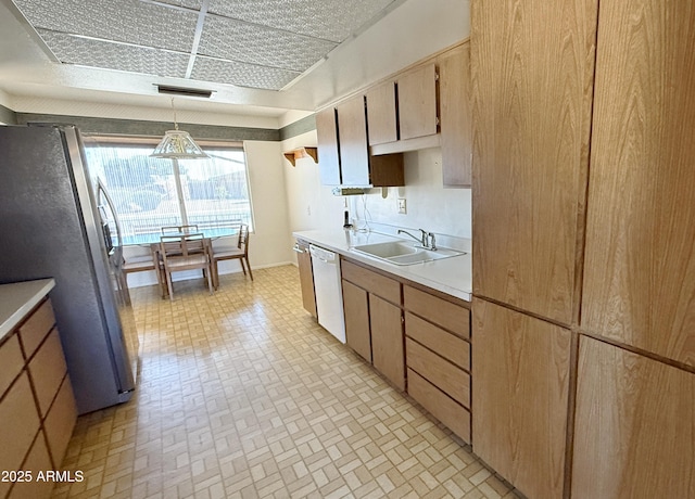 kitchen featuring freestanding refrigerator, white dishwasher, light countertops, pendant lighting, and a sink