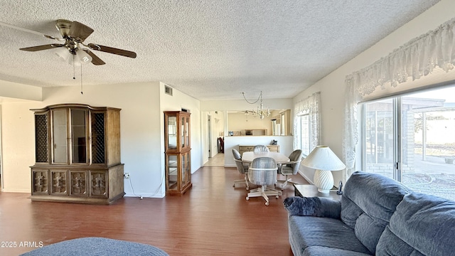 living room featuring dark wood-type flooring, visible vents, a textured ceiling, and ceiling fan with notable chandelier