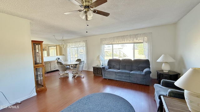 living room featuring dark wood-style floors, a textured ceiling, a wealth of natural light, and ceiling fan with notable chandelier