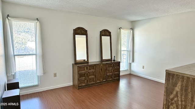 unfurnished room with dark wood-style floors, a textured ceiling, plenty of natural light, and baseboards