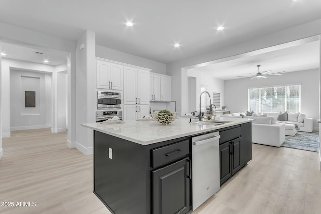 kitchen with appliances with stainless steel finishes, light wood-type flooring, sink, white cabinetry, and an island with sink