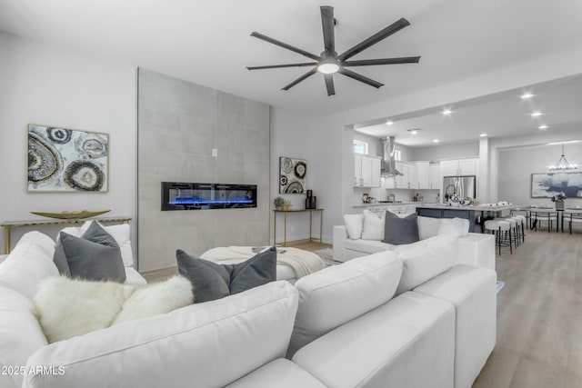 living room featuring a tile fireplace, ceiling fan, and light wood-type flooring