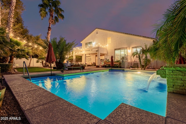 pool at dusk featuring pool water feature and a patio area