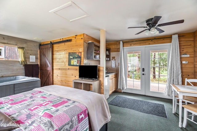 carpeted bedroom with french doors, access to outside, a barn door, ceiling fan, and wooden walls