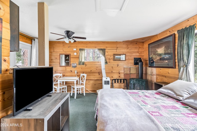 carpeted bedroom with multiple windows, ceiling fan, a wood stove, and wooden walls