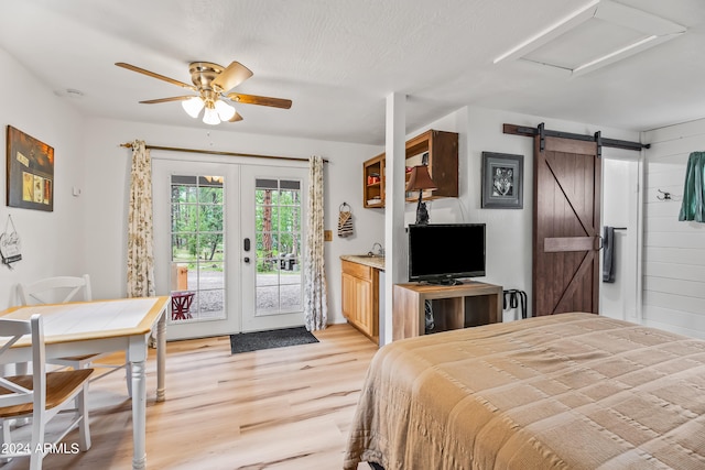 bedroom with a textured ceiling, light hardwood / wood-style flooring, access to exterior, a barn door, and ceiling fan