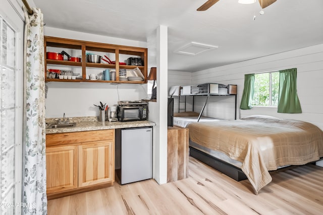 bedroom with wood walls, ceiling fan, light hardwood / wood-style floors, and stainless steel refrigerator