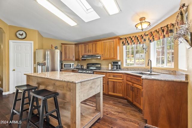 kitchen featuring stainless steel appliances, a kitchen island, sink, light stone countertops, and dark hardwood / wood-style floors