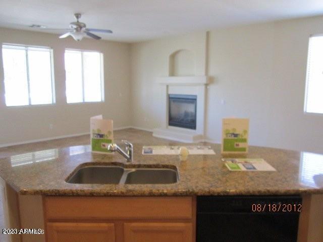 9018 W Superior Ave, Tolleson, AZ 85353 - kitchen with black dishwasher, open floor plan, light stone countertops, a glass covered fireplace, and ceiling fan