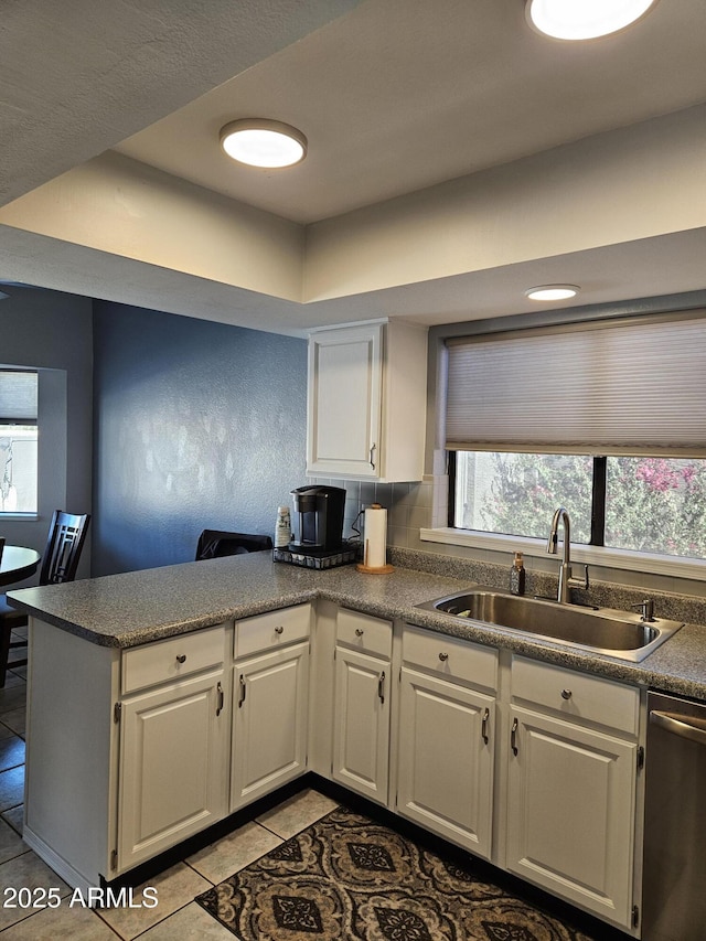 kitchen featuring white cabinets, sink, kitchen peninsula, light tile patterned flooring, and stainless steel dishwasher