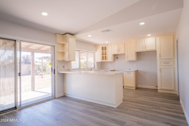 kitchen with light wood-type flooring, vaulted ceiling, kitchen peninsula, and white cabinetry