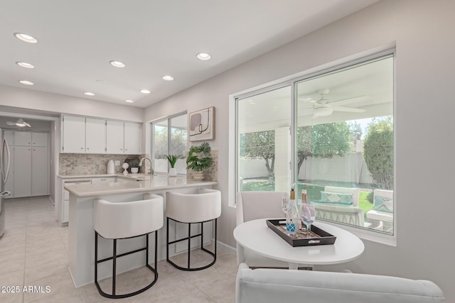 kitchen with a breakfast bar, tasteful backsplash, white cabinets, light tile patterned floors, and kitchen peninsula