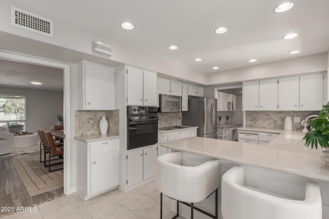 kitchen with sink, a breakfast bar area, white cabinetry, stainless steel appliances, and kitchen peninsula