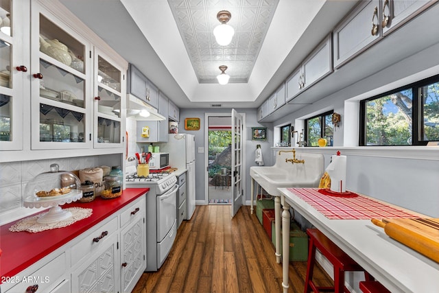 kitchen featuring a raised ceiling, a wealth of natural light, white cabinetry, and white appliances