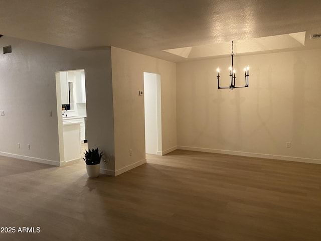 empty room with hardwood / wood-style flooring, a notable chandelier, and a textured ceiling