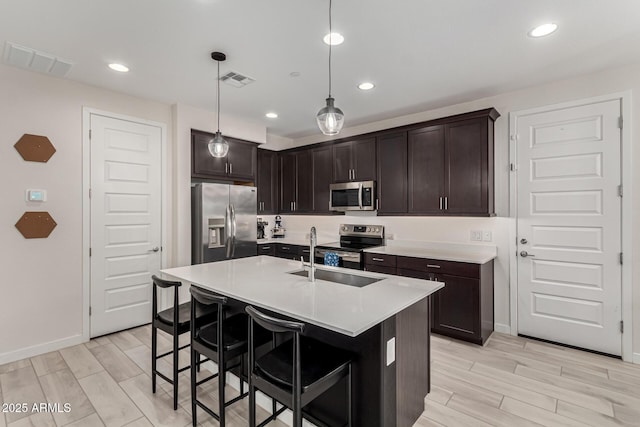 kitchen featuring a center island with sink, sink, hanging light fixtures, dark brown cabinetry, and stainless steel appliances