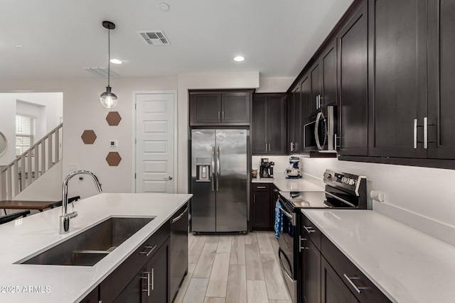 kitchen featuring appliances with stainless steel finishes, dark brown cabinets, sink, decorative light fixtures, and light hardwood / wood-style flooring