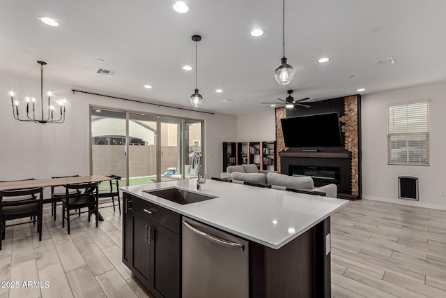 kitchen featuring a large fireplace, dishwasher, sink, an island with sink, and ceiling fan with notable chandelier