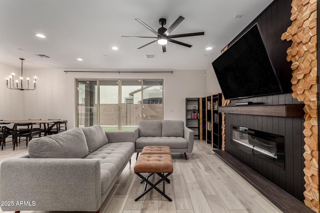 living room with ceiling fan with notable chandelier, a fireplace, and light hardwood / wood-style flooring